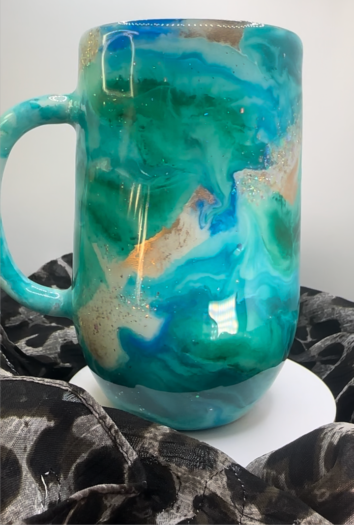 Turquoise tumbler with swirling blue, white, and gold accents, featuring a glossy finish, displayed on a white stand with black fabric.